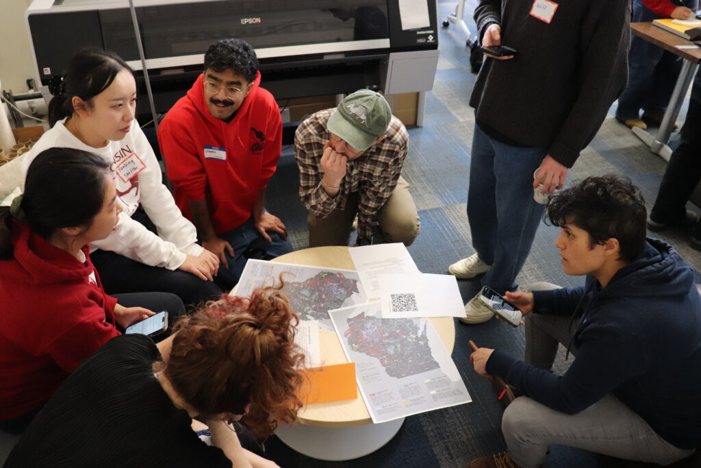 Seven people stand or sit aorund a table full of maps of Wisconsin